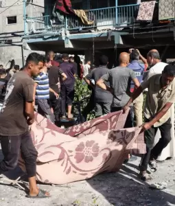 فلسطينيون ينقلون أحد ضحايا المجزرة بحق النازحين في مدرسة الجاعوني بمخيم النصيرات