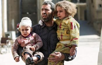 رجل يحمل طفلين جريحين أصيبا في القصف الجوي (أ ف ب)