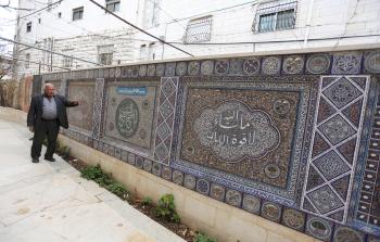 محمد الجعبري بجانب لوحات فسيفساء زين بها فناء منزله (الأناضول)