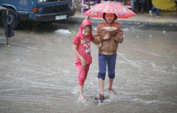 طفلان يعبران الطريق بعد أن غمرته مياه الأمطار في غزة أمس (تصوير / محمود أبو حصيرة)