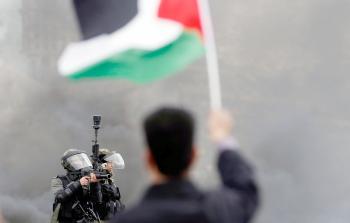 أحد جنود الاحتلال يوجه سلاحه إلى مواطن يرفع علم فلسطين خلال المواجهات في الضفة أمس (أ ف ب)