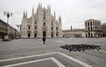 امرأة تعبر ساحة دومو الايطالية الشهيرة وهي فارغة تقريبًا في وسط مدينة ميلانو  (وكالات)