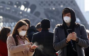 شابان من السياح بأقنعة واقية ضد الفيروس التاجي في شارع تروكاديرو أمام برج إيفل بالعاصمة الفرنسية (أرشيف)