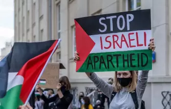 متظاهرة أجنبية ترفع علم فلسطين خط أوسطه أوقفوا الأبارتايد