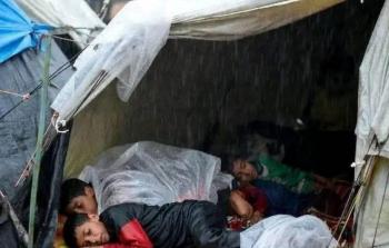 أطفال يفترشون الأرض المبللة ويغطّون أجسادهم النحيلة بأكياس، تحت الأمطار الغزيرة التي تغمر قطاع غزة