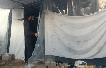 النازح رامي أبو العون يقف أمام خيمته بحثًا عن الدفء من أشعة الشمس