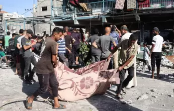 فلسطينيون ينقلون أحد ضحايا المجزرة بحق النازحين في مدرسة الجاعوني بمخيم النصيرات