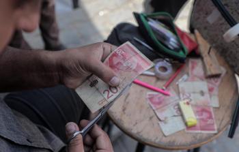 مواطن يصلح أوراق مالية مهترئة في غزة جراء نقص السيولة