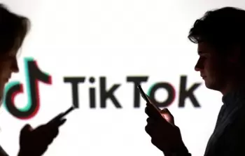 اشخاص يستخدمون هواتفهم أمام شعار تك توك (أرشيف)