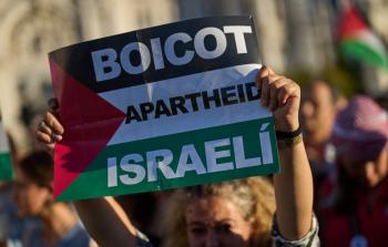 شابة ترفع علما فلسطينيا يتوسطه كلمات قاطعوا نظام الفصل العنصري الإسرائيلي