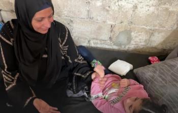 أم عمر تجلس بجوار طفلتها التي تعاني من شلل دماغي
